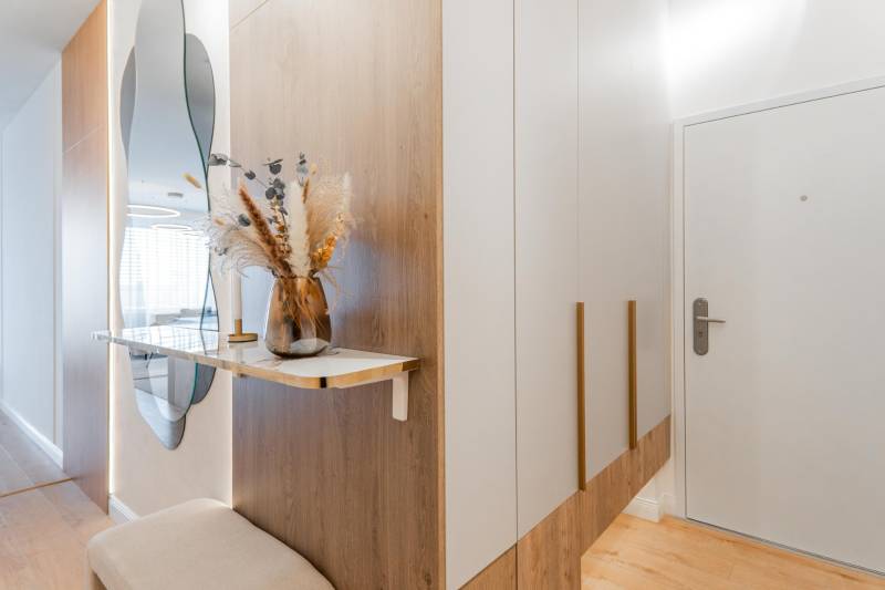 Előszoba tükörrel, szekrénnyel és dekorációval egy háromszobás lakásban, fa mintázatú padlóval.