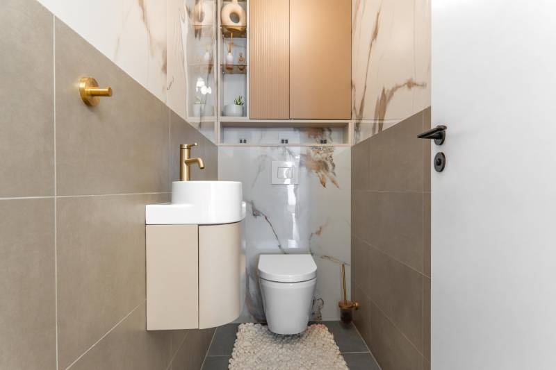 WC mosdókagylóval, arany csaptelep és márványmintás csempe egy háromszobás lakásban.