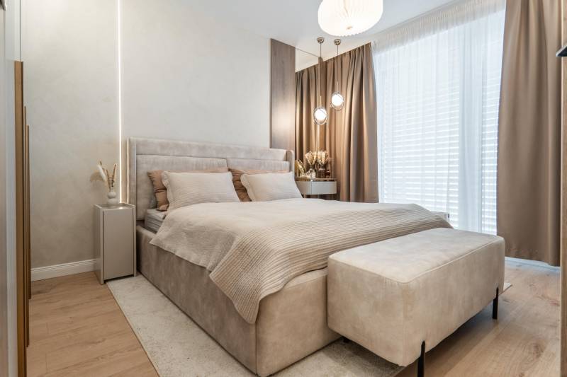 Világos hálószoba kényelmes ággyal, bézs függönyökkel és fa dekorációjú padlóval.