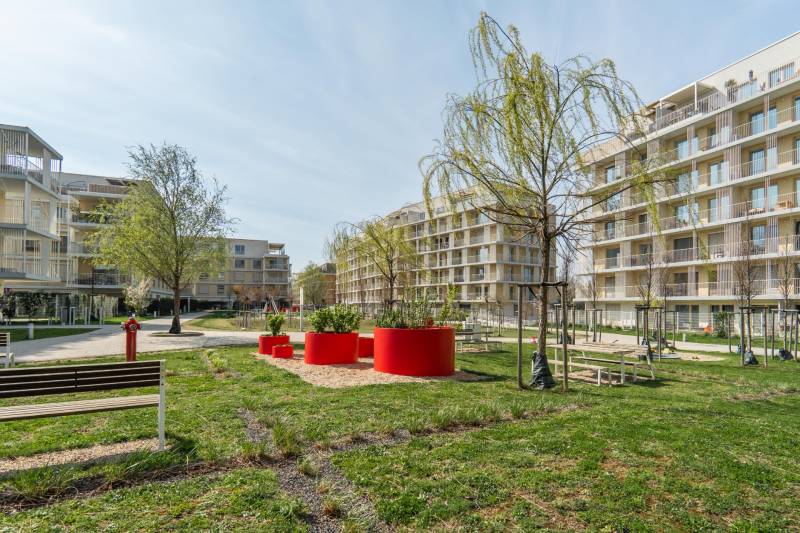 Pozsony-Ružinov lakóépületeinek külső része fákkal és padokkal.