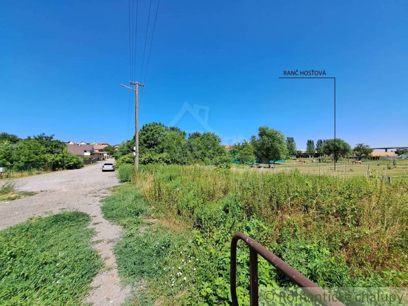 Az út a Hosťová-i telkekhez vezet, kilátással a zöldre és házakra.