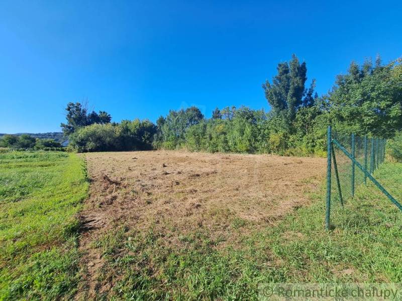 Lakótelek Hosťovában kerítéssel és környező zöldterülettel a kék ég alatt.