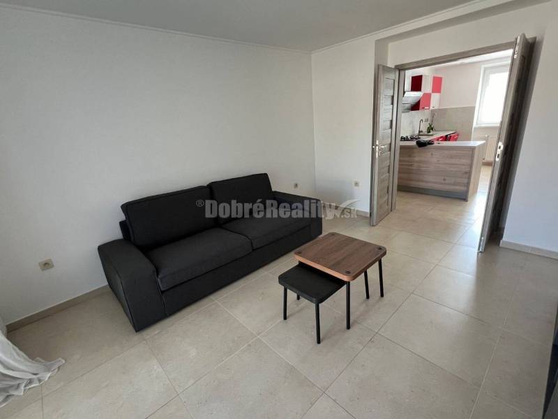 Nappali egy kétszobás lakásban fekete kanapéval és kis asztallal.