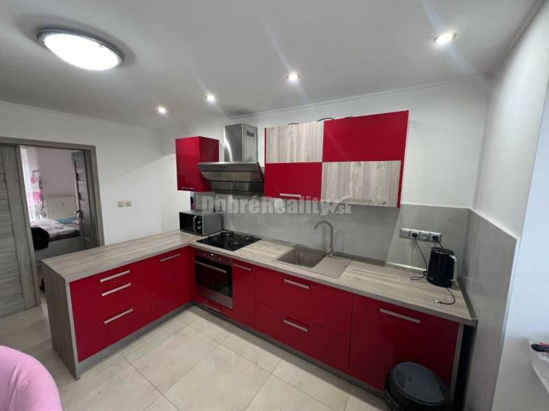 Konyha piros szekrényekkel és fa dekor padlóval egy kétszobás lakásban.