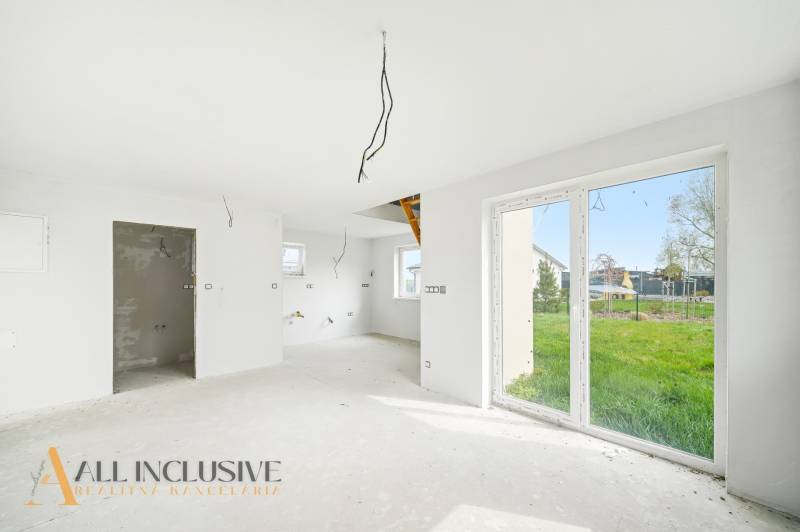 Egy berendezés nélküli házikó belső tere nagy ablakokkal és kilátással a kertre.