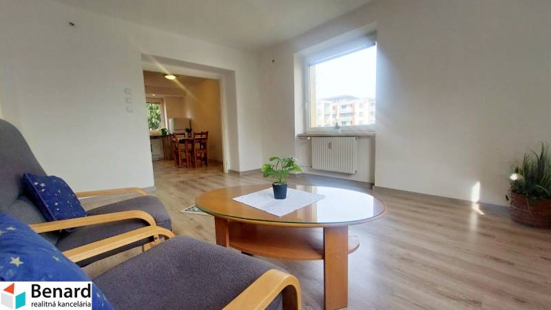 Nappali egy kétszobás lakásban ablakkal, fa dekor padlóval és asztallal, amelyen egy növény van.