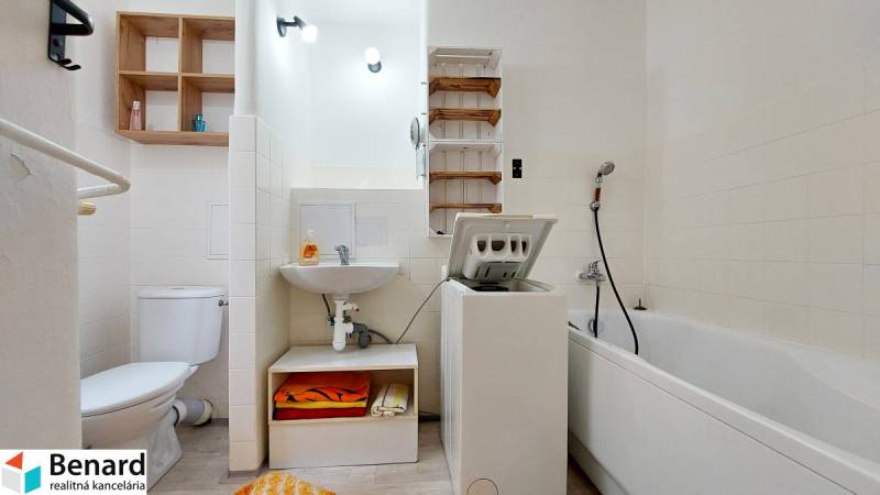 Fürdőszoba egy kétszobás lakásban zuhanyzóval, mosógéppel, WC-vel és mosdóval.