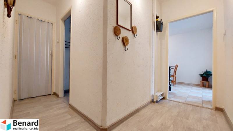 Folyosó egy kétszobás lakásban fehér falakkal és fa dekoros padlóval.