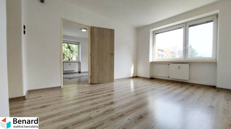 Kétszobás lakás fa mintázatú padlóval, nagy ablakkal és fehér falakkal.