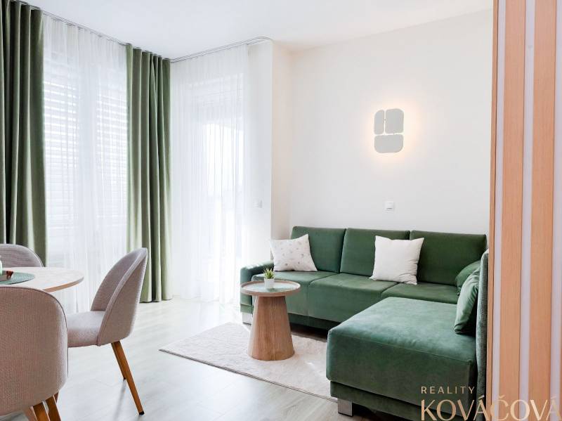 3 szobás lakás zöld kanapéval, függönyökkel és fa hatású padlóval.