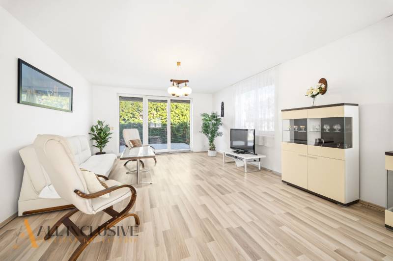 Világos nappali fa mintázatú padlóval, kanapé, fotel és televízió.