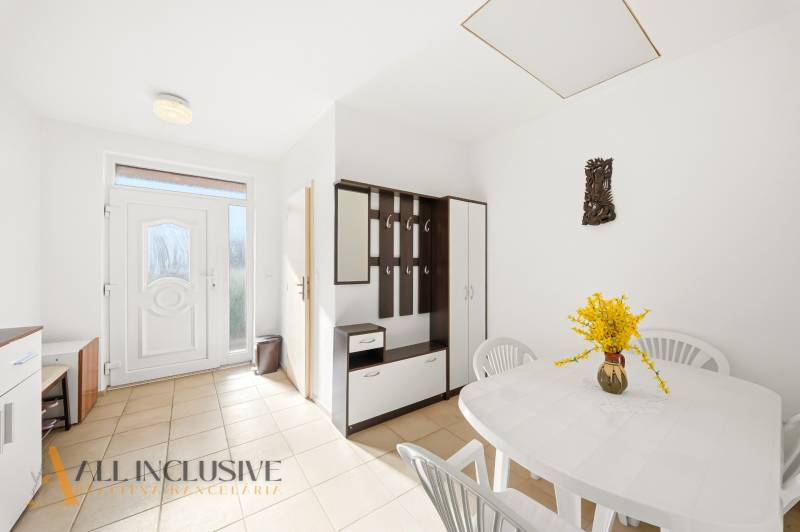 Családi ház belső tere fehér asztallal, műanyag székekkel és fogasfallal.