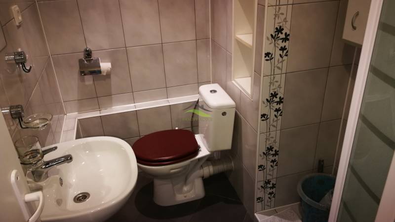Fürdőszoba a garzonlakásban WC-vel, mosdóval és virágmintás csempékkel.