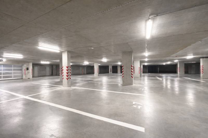 Tágas garázsok kijelölt parkolóhelyekkel, világos világítással, beton oszlopokkal.