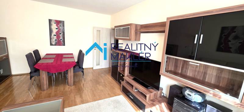 Nappali egy háromszobás lakásban, fa dekorációjú bútorokkal és padlóval.