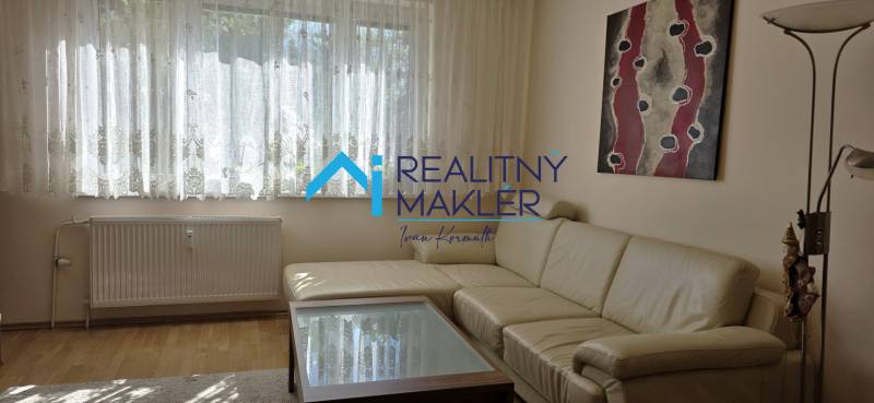 Világos nappali egy háromszobás lakásban kanapéval, absztrakt festménnyel és fa dekorációjú padlóval.