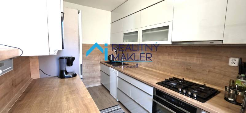 Konyha egy háromszobás lakásban fa dekorációjú konyhapulttal és padlóval.