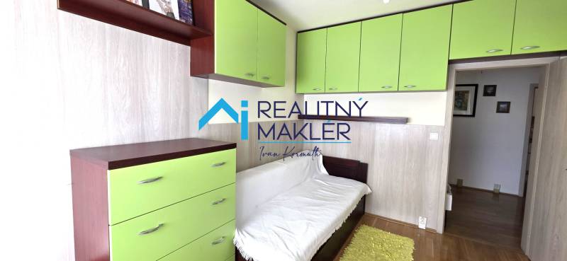 Szoba egy háromszobás lakásban fehér kanapéval, zöld szekrényekkel és fa dekoros padlóval.