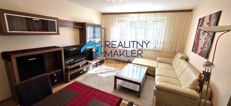 Nappali bézs kanapéval és sötét fa bútorokkal egy háromszobás lakásban.