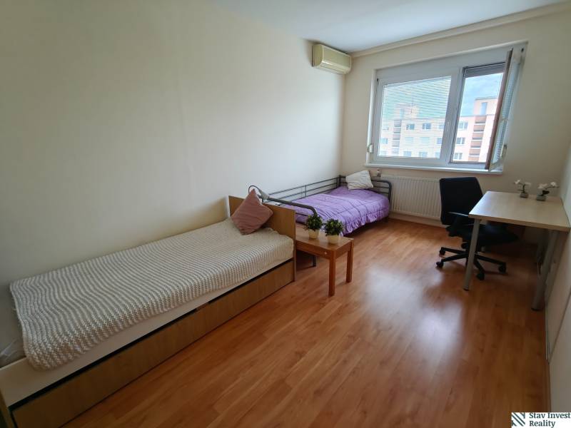 Szoba egy háromszobás lakásban két ággyal, íróasztallal és fa dekorációjú padlóval.