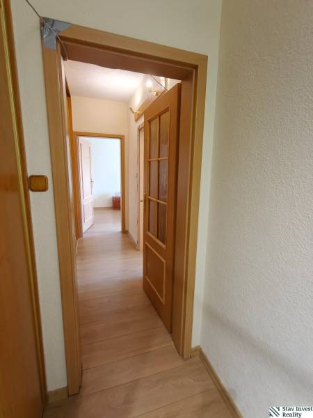 Folyosó ajtókkal és fa dekorációjú padlóval egy háromszobás lakásban.