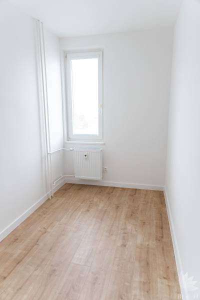 Szoba egy háromszobás lakásban, ablakkal és fa mintázatú padlóval.