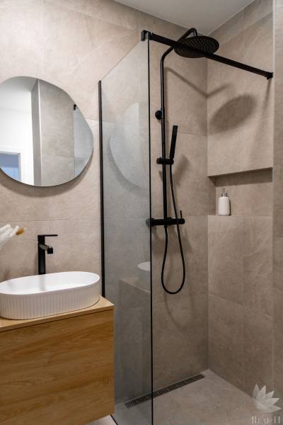 Fürdőszoba egy háromszobás lakásban mosdóval és zuhanyzóval fekete csapokkal.