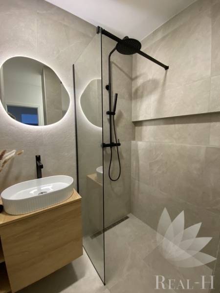 Fürdőszoba mosdóval, zuhanyzóval és tükörrel egy háromszobás lakásban.