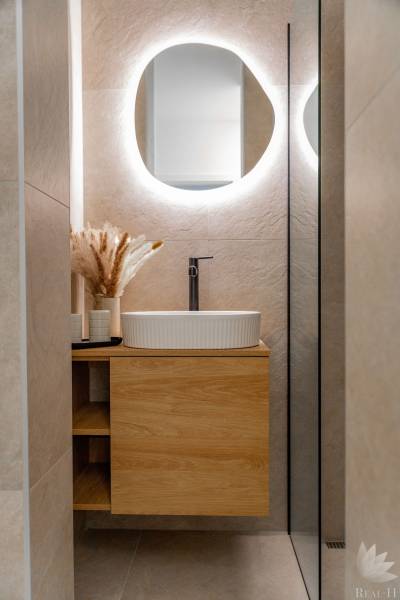 Fürdőszoba egy háromszobás lakásban, mosdókagylóval egy fa szekrényen és világítással ellátott tükörrel.