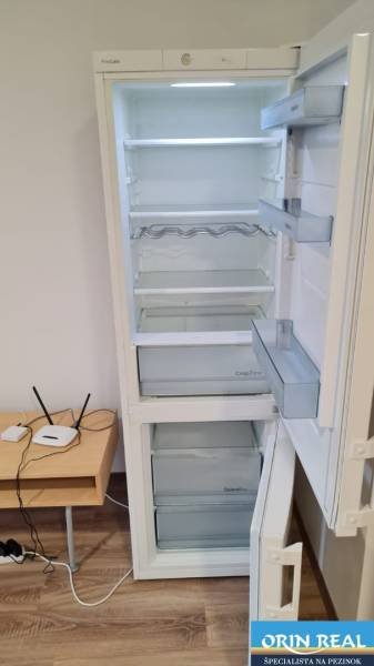 Hűtőszekrény kinyitása egy garzonlakásban fa mintázatú padlóval és kis asztallal.