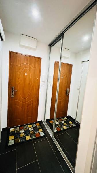 Folyosó egy 3 szobás lakásban ajtókkal, tükrös szekrénnyel és színes szőnyeggel.