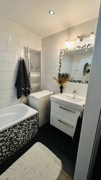 Elegáns fürdőszoba csempékkel, mosdóval és káddal, a háromszobás lakás része.
