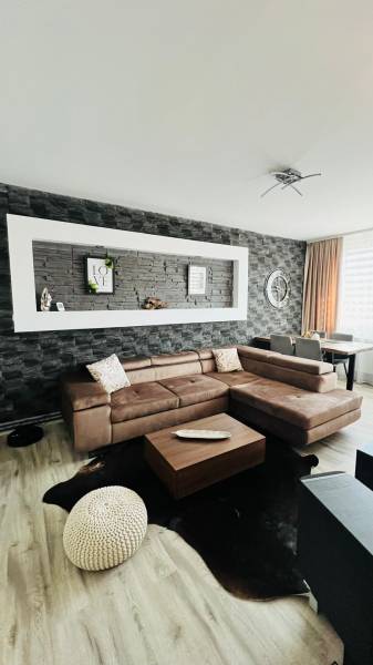 Nappali egy háromszobás lakásban, fa mintázatú padlóval és sarok ülőgarnitúrával.