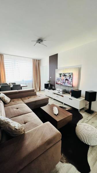 Nappali sarokkanapéval, TV állvánnyal és fa mintázatú padlóval.