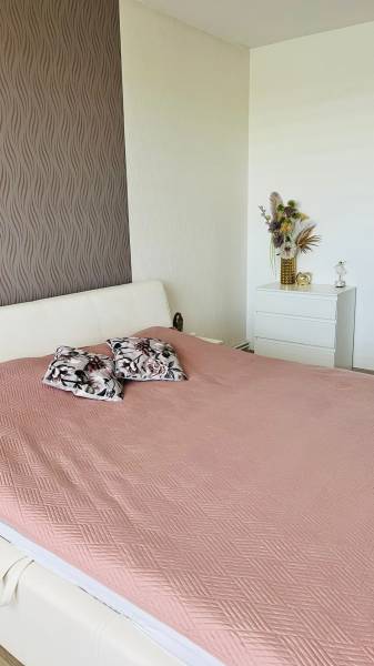 Hálószoba egy háromszobás lakásban ággyal, dekoratív párnákkal és díszes tapétával.