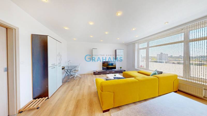 Nappali egy kétszobás lakásban fa mintázatú padlóval és sárga kanapéval.