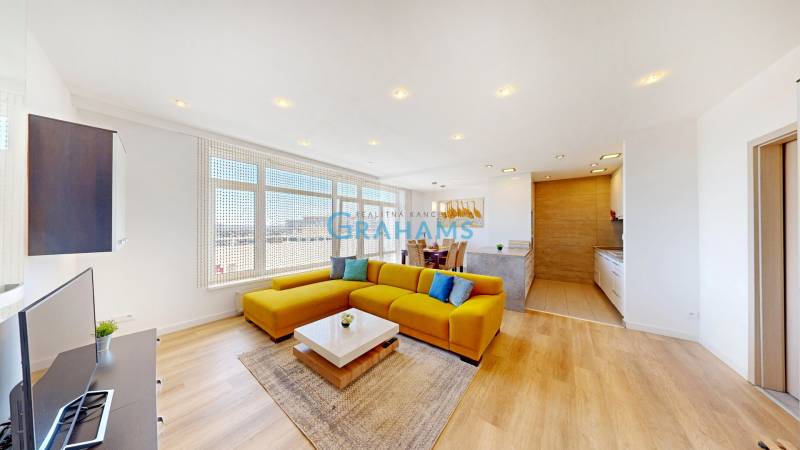 Világos nappali kanapéval, étkezőasztallal és fa mintázatú padlóval egy kétszobás lakásban.