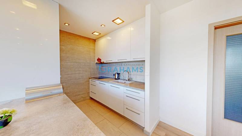 Konyha egy kétszobás lakásban fehér szekrényekkel és fa mintázatú padlóval.