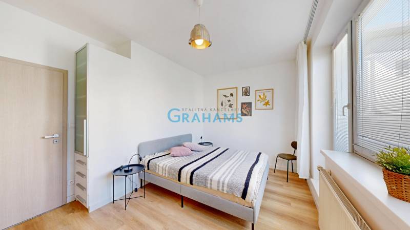 Hálószoba egy kétszobás lakásban ággyal, éjjeliszekrénnyel és fa dekoros padlóval.