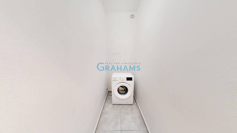 Keskeny helyiség mosógéppel egy kétszobás lakásban, fehér falak, csempe a padlón.