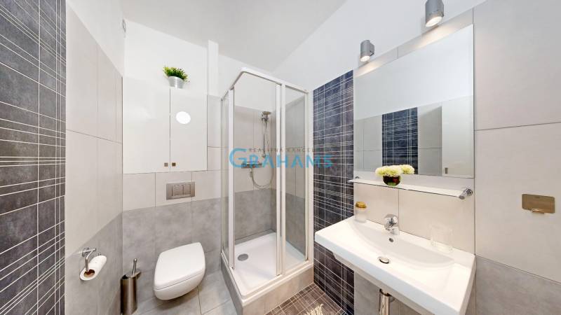 Fürdőszoba egy kétszobás lakásban zuhanyzóval és modern szürke színű csempével.