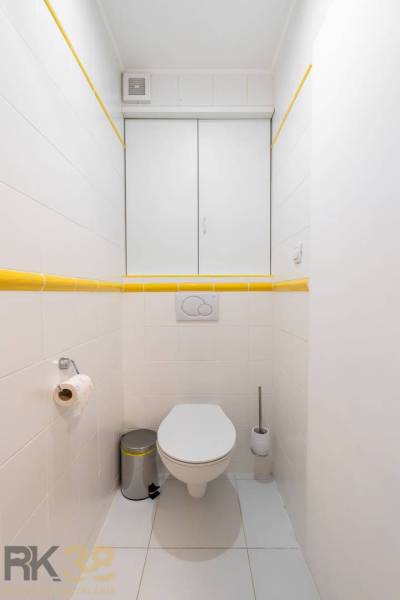 Fürdőszoba fehér csempékkel és sárga részletekkel a Nyaraló apartmanban.