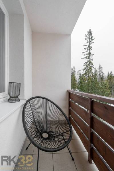 A poprádi rekreációs apartman erkélye fekete székkel és kilátással a fákra.