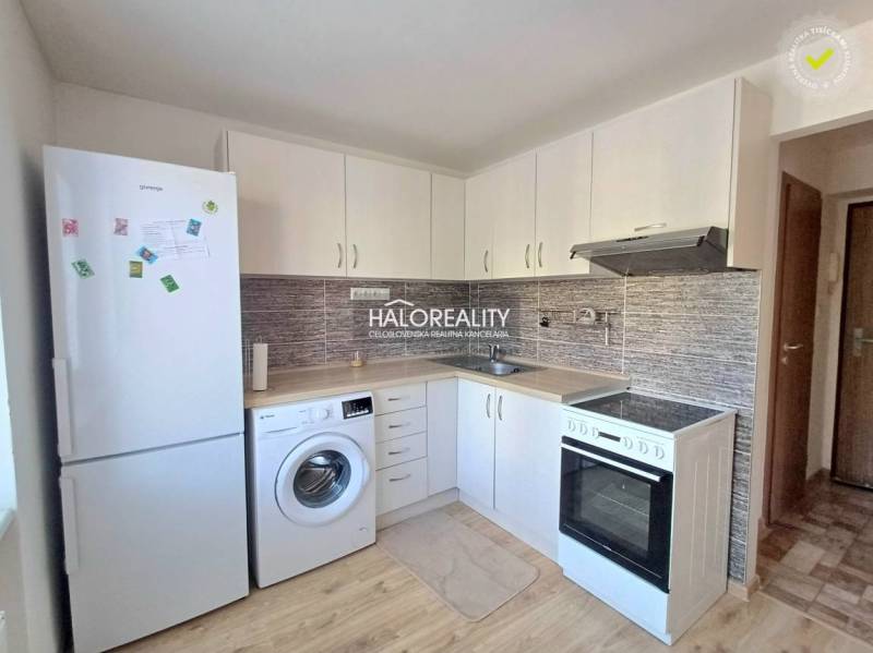 Konyha egy egyszobás lakásban fehér szekrényekkel és fa dekorációjú padlóval.