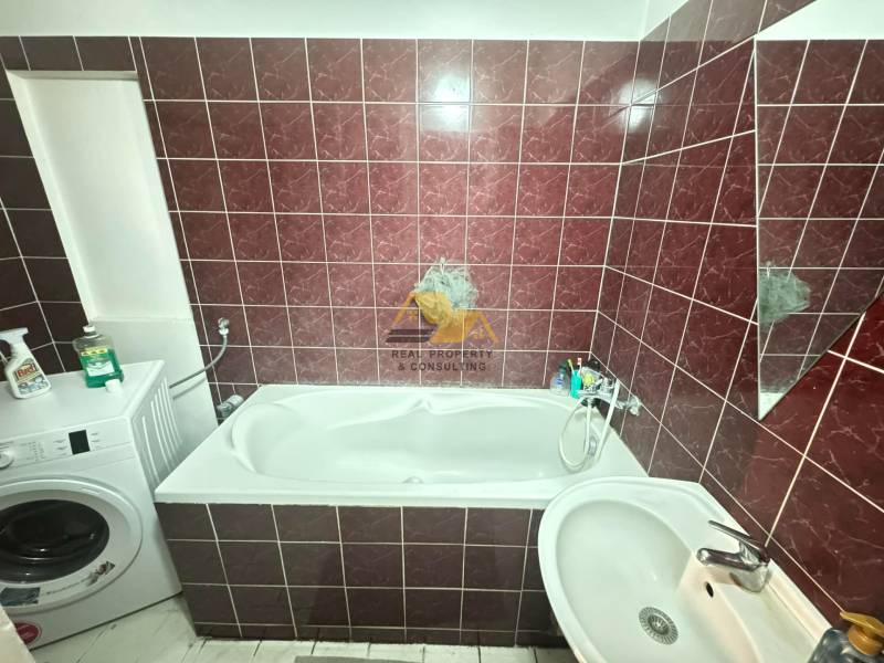 Fürdőszoba egy kétszobás lakásban káddal, mosógéppel és sötétvörös csempével.