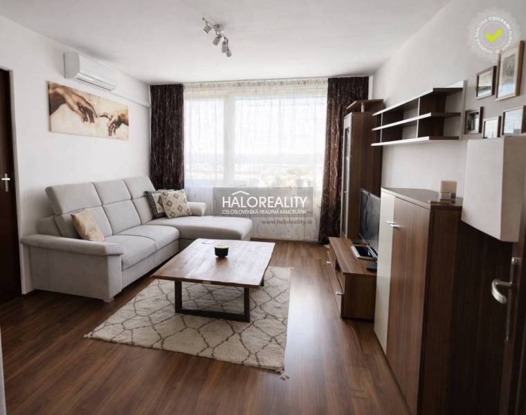 Nappali egy négy szobás lakásban, fa mintázatú padlóval, kanapéval és televízióval.