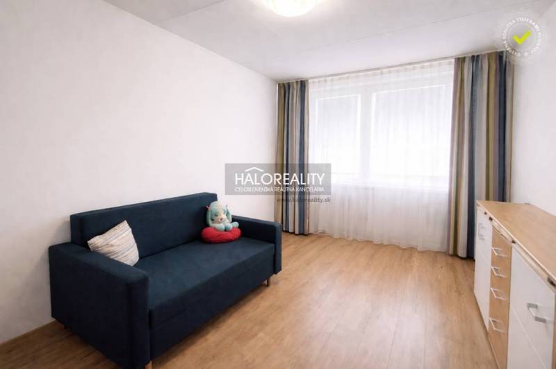 Szoba egy négy szobás lakásban kék kanapéval és fa mintázatú padlóval.