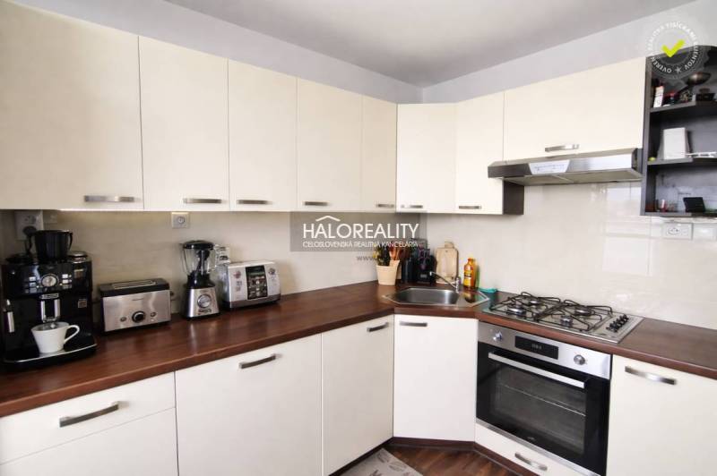 Konyha egy 4 szobás lakásban fehér szekrényekkel és fa hatású padlóval.