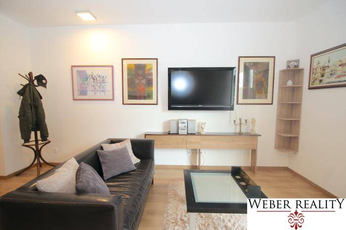 Nappali egy egyszobás lakásban fekete kanapéval és fa padló dekorációval.