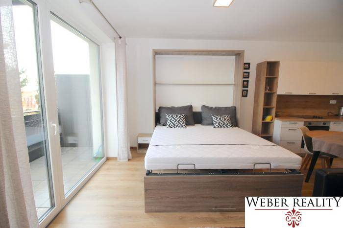 Hálószoba kihúzható ággyal és fa dekorációjú padlóval egy egyszobás lakásban.